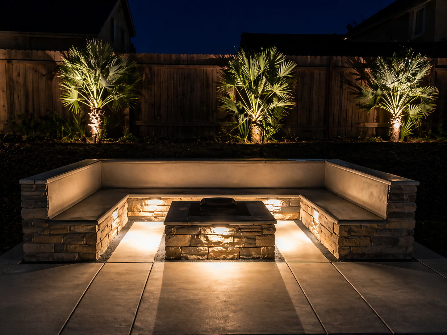 Built-in stone bench and fire pit with uplit palms at night