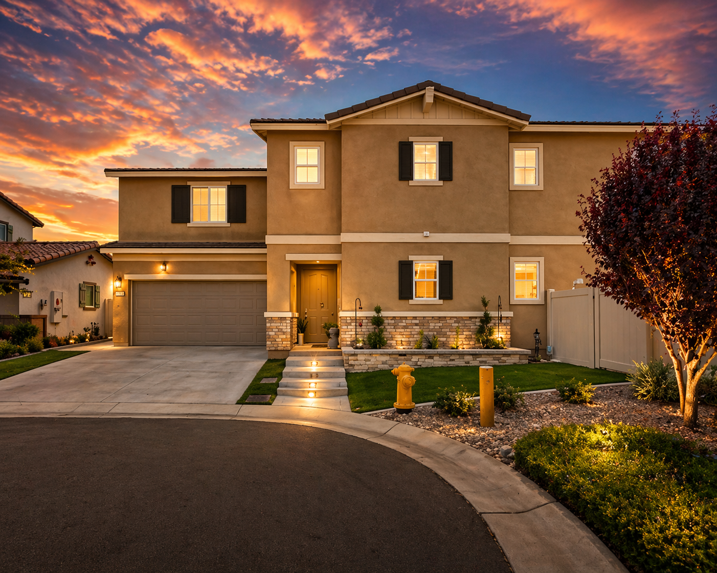 Two-story home at sunset with stone-veneer planter, path lighting, and xeriscape front yard